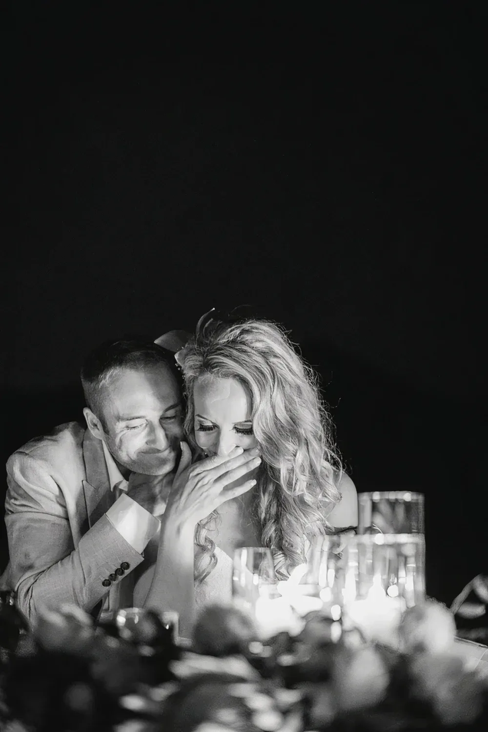 A couple shares a tender moment during their engagement at Silvara Cellars, with the man leaning close to the woman who covers her mouth, both smiling softly against a dark background.