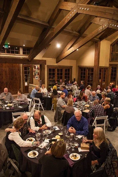 A lively group dinner event at Silvara Cellars in Leavenworth with people seated at round tables enjoying food and conversation inside a rustic wooden-beamed venue.