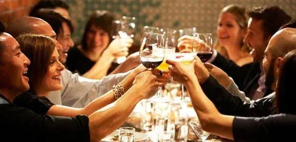 A group of people sitting around a table raising their glasses in a toast, smiling and enjoying a celebratory moment indoors.