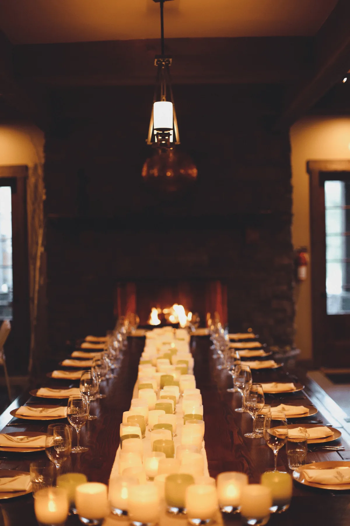 Long candlelit dinner table set inside Silvara Cellars, leading to a lit stone fireplace