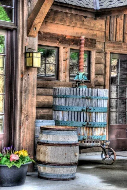 Wooden wine press and barrels outside a rustic wine tasting room with wooden walls and windows reflecting greenery.