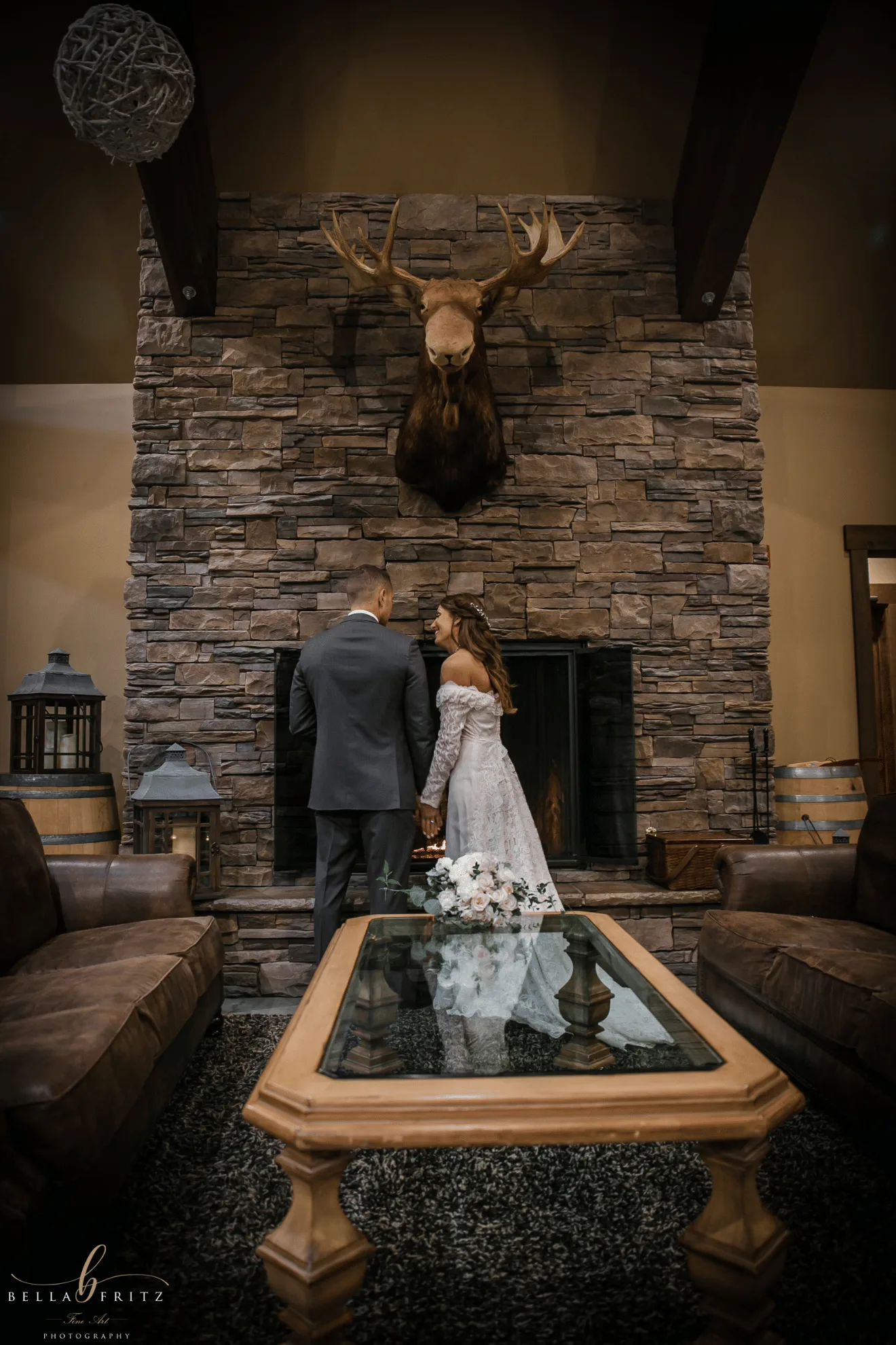 Bride and groom holding hands before the stone fireplace inside Silvara Cellars, beneath a mounted moose head