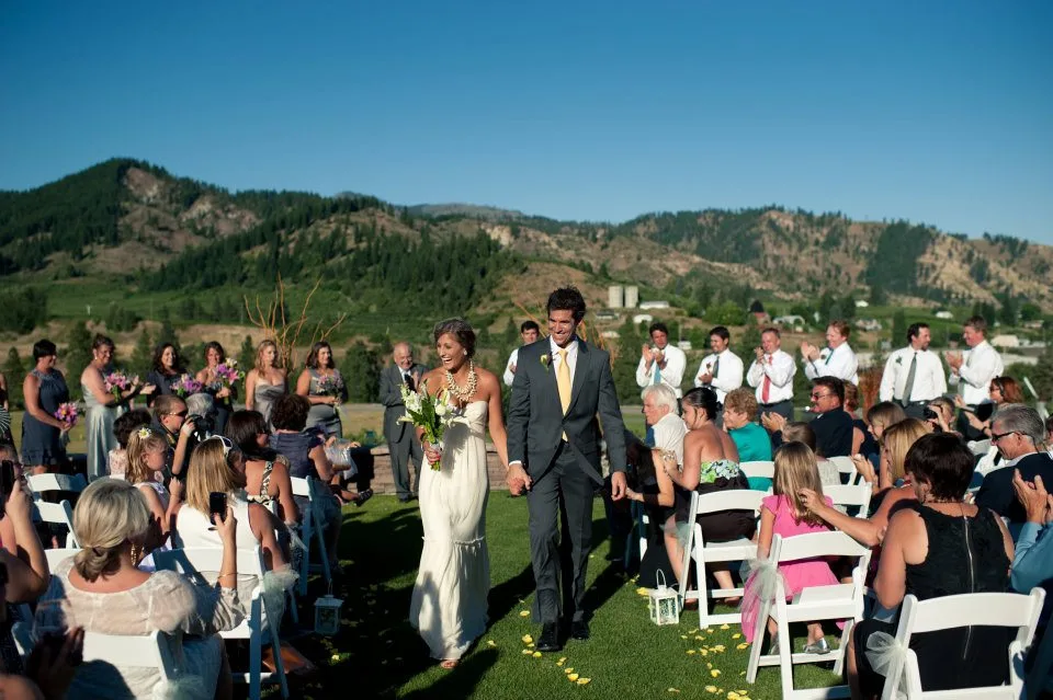 Bride and groom walking toward the camera as guests take in the mountain view at Silvara Cellars in Leavenworth, WA
