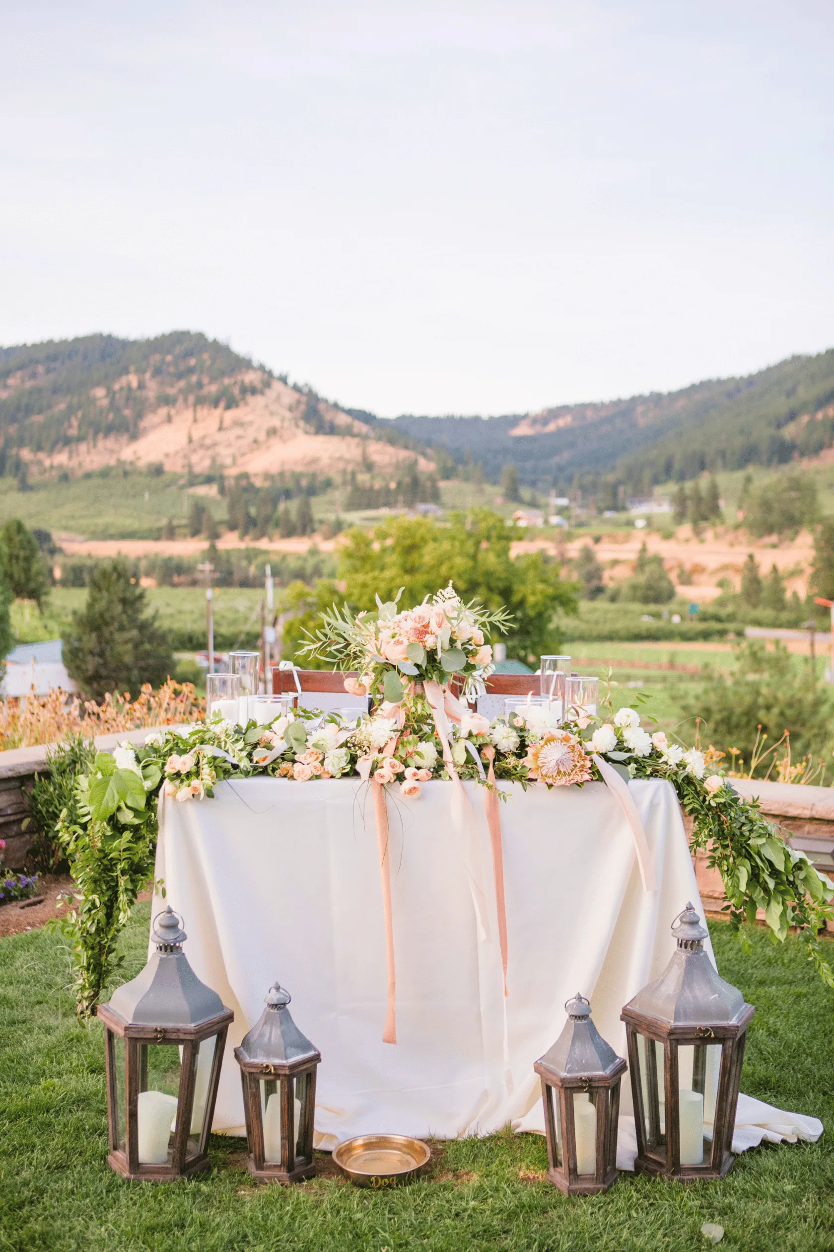 Sweetheart table draped in flowers and ribbon, ringed by lanterns on the lawn at Silvara Cellars above the valley