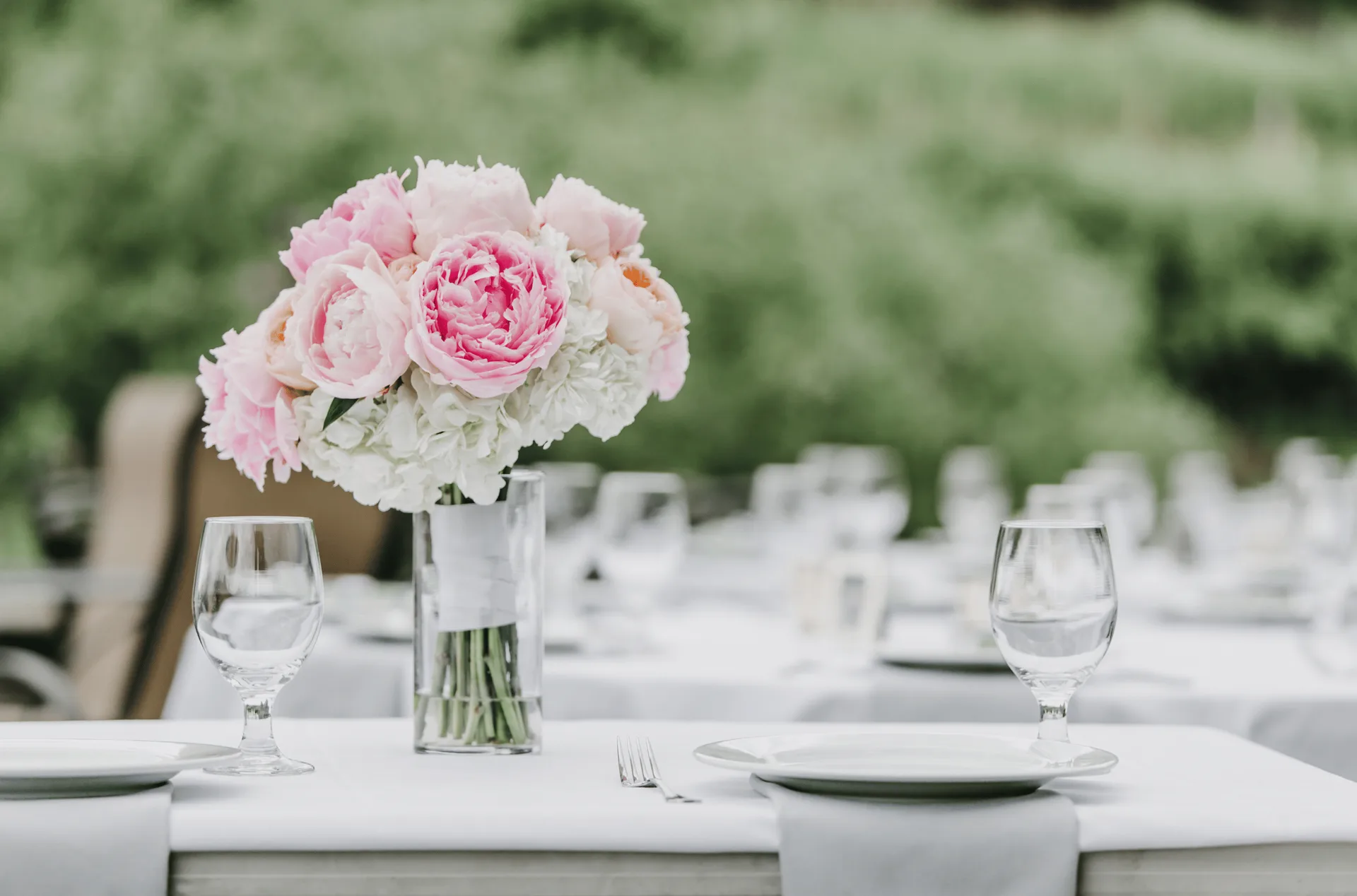Pink peony centerpiece on a white-clothed reception table set outdoors at Silvara Cellars