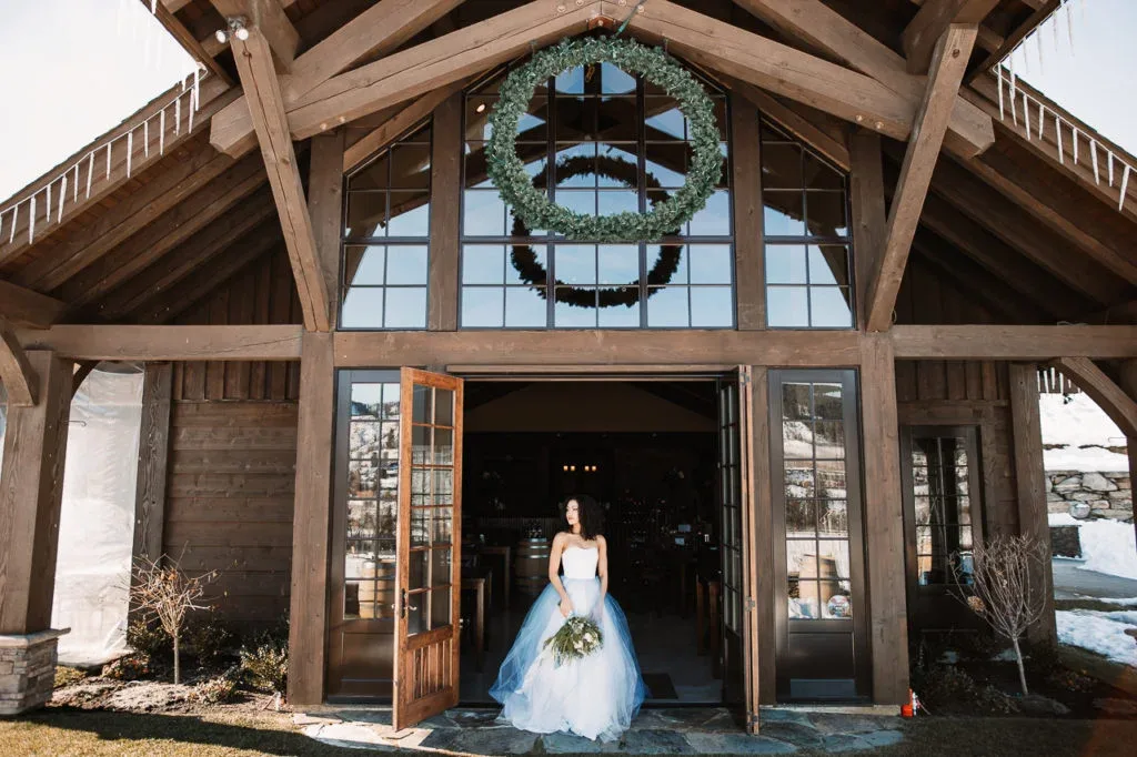 Bride standing outside the Silvara Cellars winery in winter, with a large wreath hanging above the entrance