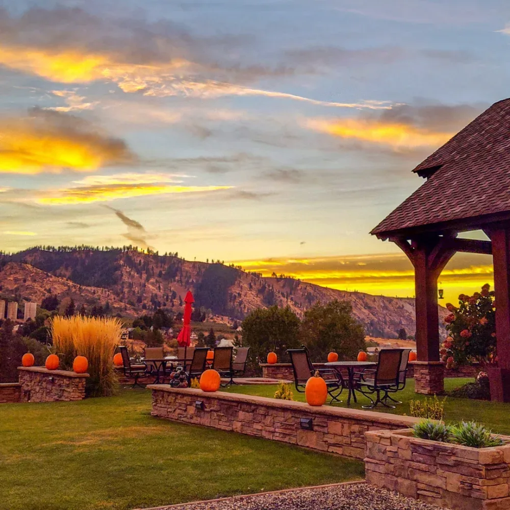 Outdoor seating area with tables, chairs, and pumpkins on stone walls during sunset in a mountainous rural setting.